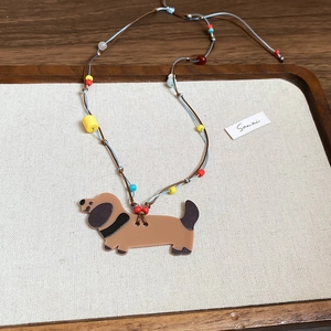 Detail of dachshund puppy pendant with colorful beads and woven necklace cord on beige fabric