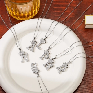 Silver crown letter necklaces with rhinestones on a white ceramic plate over dark wood