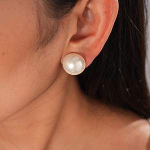 Close-up of a large white pearl stud earring worn by a model in a minimalist style