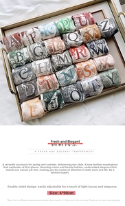 Detail showing various patterned letter silk scarves in a gold tray measuring 6x98cm