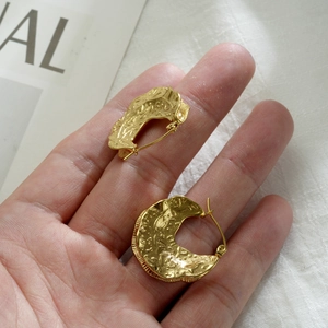 Detail of gold-plated irregular oval earrings featuring a handmade hammered lava texture