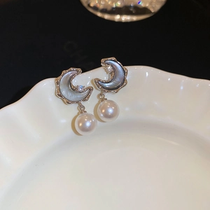 Macro shot of silver moon earrings with dark resin inlay and elegant white pearls