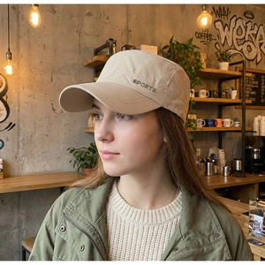 Detail of beige cadet cap with laser-cut side vents and SPORTS embroidery in a cafe