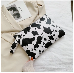 Detail of cow print clutch bag with wrist strap on neutral fabric background