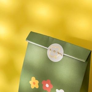 Green floral paper gift bag with flower sticker seal on warm yellow background