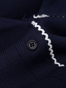 Macro shot of navy knit cardigan with white scalloped trim and black button detail