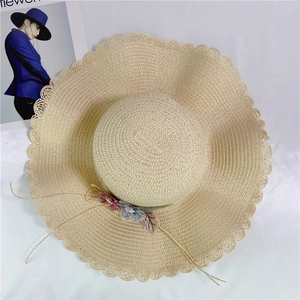 Detail of beige straw hat with delicate wavy brim and fabric floral decoration