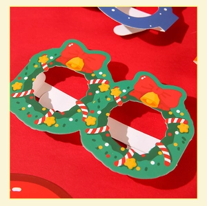 Détail de lunettes de Noël en papier avec couronne verte, nœud rouge et motifs festifs
