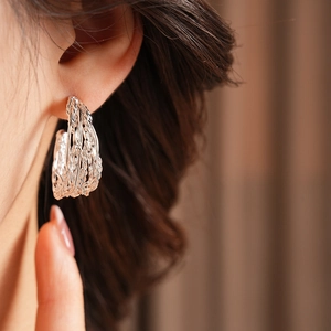 Close-up of model wearing silver multi-layer woven textured C-shaped hoop earrings