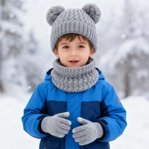 Detail of gray cable-knit kids' winter set with pom-poms, scarf, and gloves in the snow