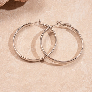Detailed view of polished silver hoop earrings with a classic pin clasp on a stone surface