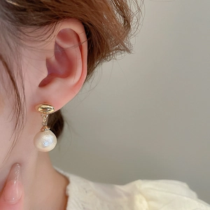 Close-up of elegant gold stud earrings with textured cotton pearl pendants on a model