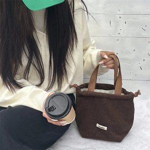 Detail of dark brown wool drawstring bag with white polka dots and woven handles