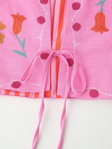 Detail of pink cotton-linen cardigan with floral embroidery and bow tie closure