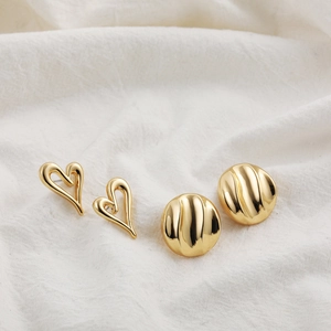 Detailed view of hollow heart and textured round 18K gold earrings on white fabric