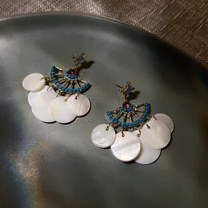 Detailed shot of gold fan-shaped earrings with blue beads and white shell disks