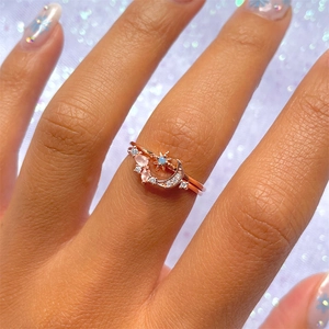 Close-up of stacked rose gold moon and star rings with pink marquise and blue stones
