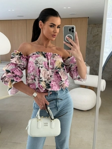 Dettaglio del top floreale rosa con spalle scoperte, jeans blu e borsa in pelle