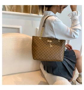 Detail of brown geometric tote bag with gold deer charm and chain strap on white sofa