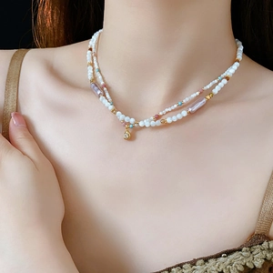 Detail of double-layer beaded necklace with faux pearls and gold pendant on model