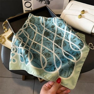 Détail d'un foulard en soie florale avec dégradé bleu-vert et motif de grille géométrique