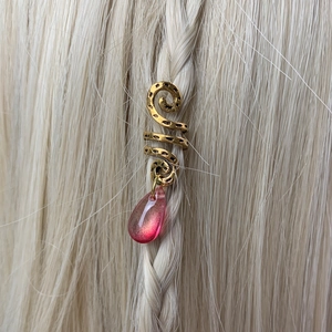 Detail of golden spiral dreadlock accessory with pink crystal charm on braided hair