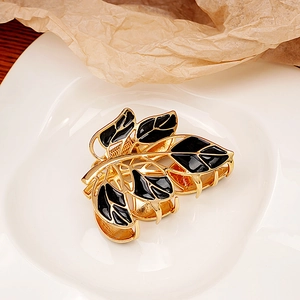 Close-up of golden leaf hair claw clip with black enamel detail on ceramic plate