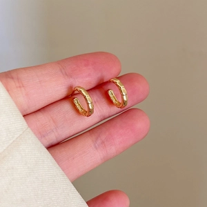 Detailed view of small gold hoop earrings with a unique bamboo texture and metallic finish