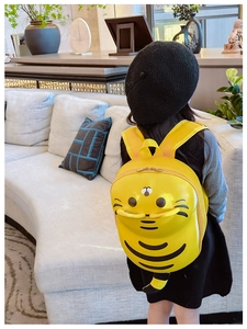 Rear view of a young girl wearing a bright yellow cartoon tiger backpack in a cozy room