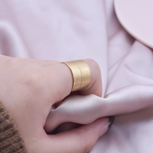 Minimalist wide braided gold stainless steel open ring worn on finger with silk background