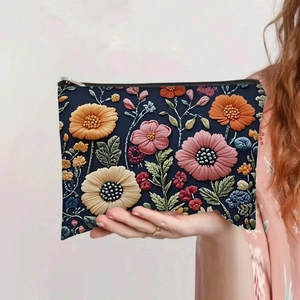 Detail of hand holding a navy blue makeup bag with vibrant 3D floral embroidery patterns