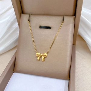 Detailed macro view of a gold bow pendant necklace in a premium brown gift box