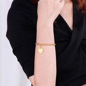 Close-up of a 18k gold-plated beaded bracelet with a heart pendant on a model's wrist