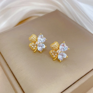 Detail of golden four-leaf clover stud earrings with heart zircons on luxury silk