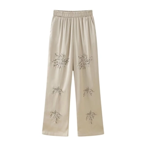 Detail of beaded floral embroidery on apricot satin wide-leg trousers with silk texture