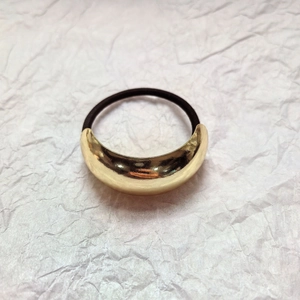 Minimalist gold arc metal hair tie with black elastic band on white texture