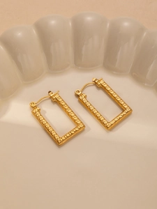 Detail of gold rectangular earrings featuring intricate engraved geometric Greek key patterns