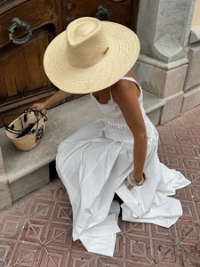 Dettaglio di un cappello di paglia beige a tesa larga con logo dorato per un look da estate
