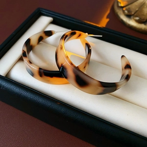 Macro shot of brown tortoiseshell C-shaped acetate earrings on jewelry box lining