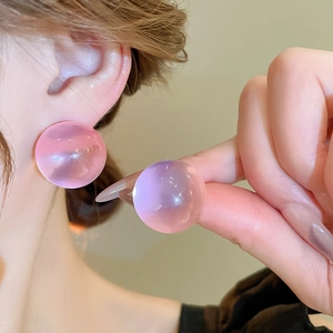 Close-up of pink transparent resin round ball stud earrings worn by a model