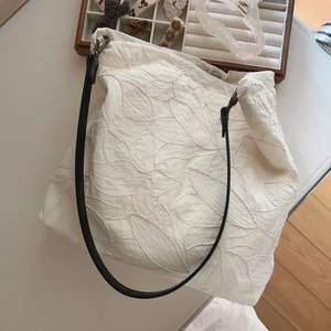 Beige embroidered canvas tote bag with black leather strap and floral leaf patterns