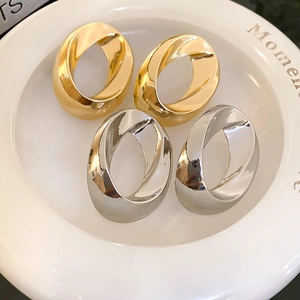 Minimalist twisted oval hoop earrings in gold and silver finish on a ceramic plate