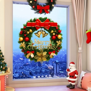 Close-up of Christmas wreath with red bow, gold bells and Merry Christmas lettering on window