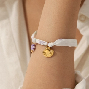 Detail of floral silk bracelet with gold shell charm and purple flower on a model wrist