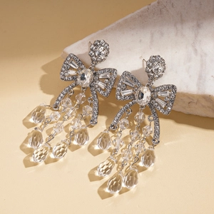 Silver bow drop earrings with sparkling rhinestones and crystal tassels on marble base