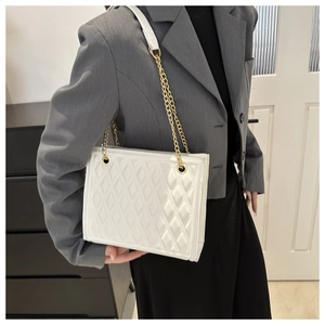 Detail of white quilted chain bag with gold metal hardware on model in grey blazer