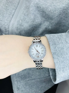Silver ladies quartz watch with diamond bezel and roman numerals on textured background