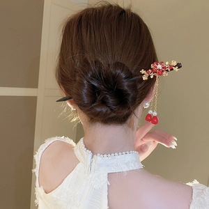 Detailed view of handmade wooden hair stick with red flowers and golden tassels on bun