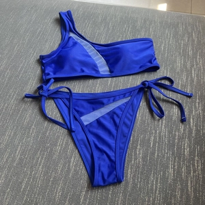 Flat lay of navy blue bikini set with one-shoulder top and sheer mesh patchwork details