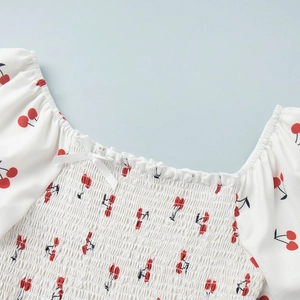 Detail of square neckline with cherry print, shirred bodice and white ribbon bow